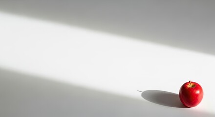 A single red apple on a white surface with a shadow cast by a light source.