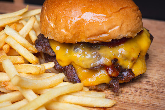 Double cheeseburger with fries on wooden board.