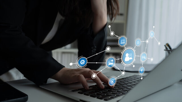A businesswoman works intently on her laptop, surrounded by digital network icons symbolizing communication and technology in a modern office space. Tessel - Powered by Adobe