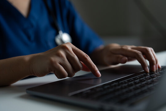 Close-up of hands of healthcare worker in blue scrubs using laptop, concept of health IT systems, medical data entry, e-health records, and digital transformation in the healthcare industry.