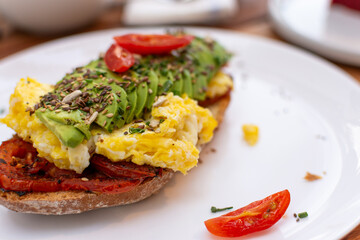 Primer plano en ángulo de bruschetta con huevos revueltos cremosos, aguacate fresco y tomates confitados. Detalle apetitoso de texturas para menú de brunch saludable.