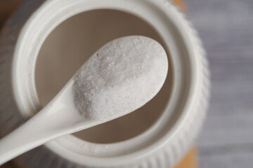 White salt on a spoon next to a jar in the kitchen