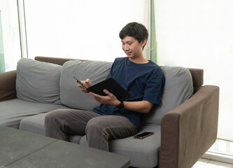 Asian Man Multitasking with Smartphone and Tablet While Sitting on the Living Room Sofa