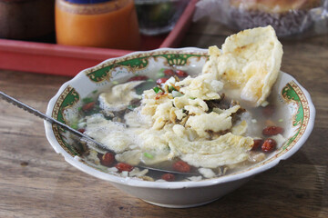 A bowl of Indonesian chicken porridge served with crackers and toppings.