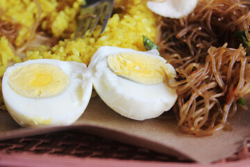 Yellow rice meal with vermicelli and boiled eggs on brown paper.