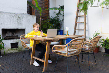 Young girl participating in video call on laptop at outdoor patio