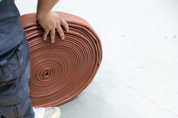 Worker's hand moving large coiled fire hose on concrete floor