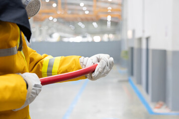 Firefighter holding hose ready to extinguish fire in factory warehouse
