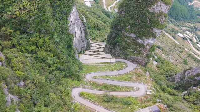 Revealing drone shot of the steep, sheer rock formations and the zigzag road carved into the cliffside at Lingpaishi, Wuxi County, China. Captures remote natural beauty and engineering.