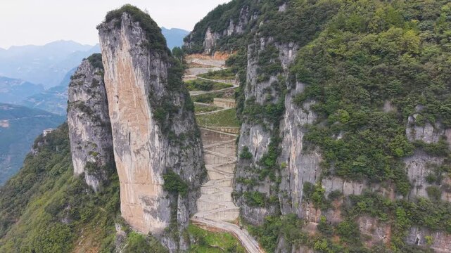 Slow orbiting drone shot of the steep, sheer rock formations and the zigzag road carved into the cliffside at Lingpaishi, Wuxi County, China. Captures remote natural beauty and engineering. UHD.