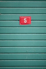 Number 5 sign on a green wooden wall in daylight