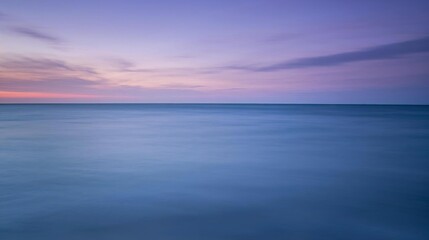 Fototapeta premium Serene seascape at twilight, where the calm, boundless ocean meets a soft gradient sky painted with gentle lavender and deep blue hues, creating a peaceful and contemplative natural vista