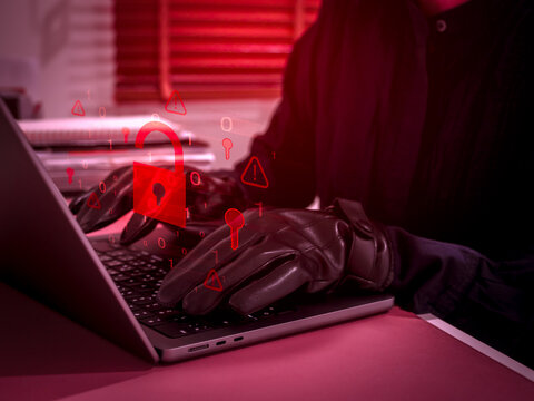 Cybersecurity threat concept showing hacker or scammer using laptop with glowing red unlocked padlock icon, representing hacking, data breach, online scam, identity theft, and digital crime activity.