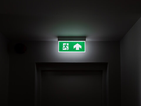 Emergency exit sign glowing in dark hallway, symbolizing building safety, fire escape route, emergency preparedness, survival path, and standard safety compliance in public and commercial buildings.