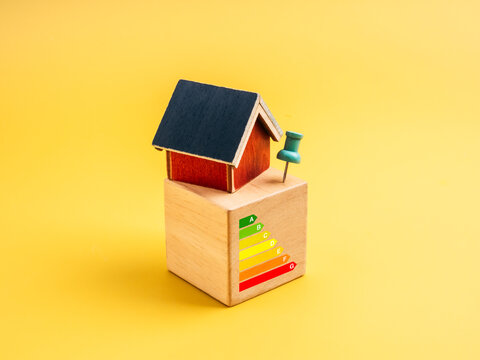 Mini house model on wooden block with energy efficiency rating scale symbolizes home energy performance, cost saving, and sustainability for green building, smart home and eco-friendly living content. - Powered by Adobe