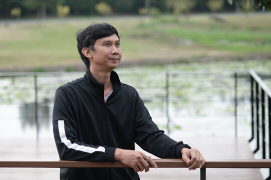 Asian Man Relaxing by the Water on a Wooden Deck, Looking Out at Nature