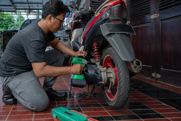 Indonesian southeast asian repairman using a green impact wrench tool to repair a motorcycle in a workshop