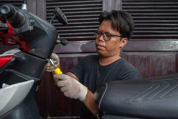 Indonesian southeast asian repairman using a socket screwdriver tool to repair a motorcycle in a...
