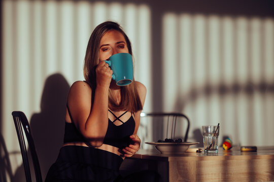 Sleepy Woman Drinking Coffee in the Morning in her Kitchen. Lady needs her caffeine boost before starting the day with energy