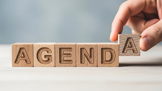 Hand arranging wooden blocks to spell out the word agenda for a business meeting
