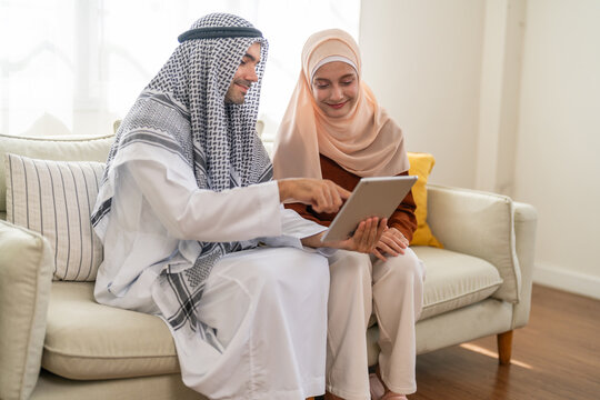 Muslim couple using tablet at home, modern islamic collaboration, learning or planning, concept of faith, family and technology online shopping, e-commerce platform, arab culture, islamic fintech