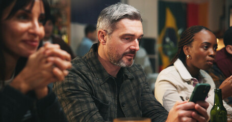 Fototapeta premium Pub, group and man with smartphone, sports betting and checking game results for online competition. Watching, match and gambling with mobile app in bar, entertainment and football fans or people