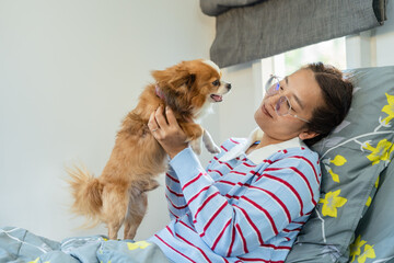 Happy Asian woman playing and holding cute Chihuahua dog on bed looking at each other with love and affection