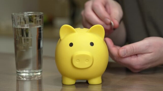 yellow piggy bank glass water hands depositing coin, close-up kitchen countertop illustrating liquid emergency fund concept, calm pragmatic mood with steady tabletop composition, adult building rainy