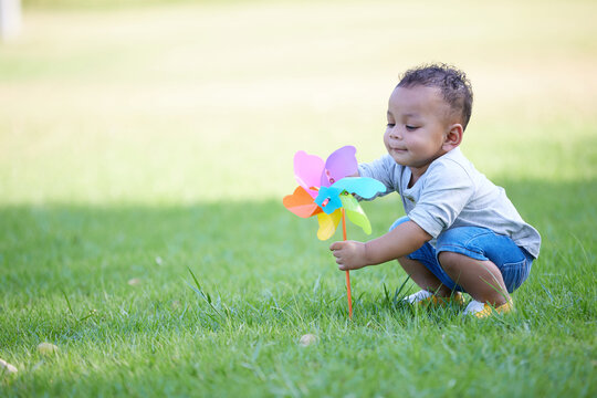 A boy enjoying a vibrant pinwheel in a park setting. He's surrounded by green grass and sunshine