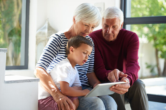 Grandparents, boy and tablet in home, relax and bonding on stairs with game, elearning or puzzle. Senior man, woman and child with tech, application and scroll with problem solving at family house