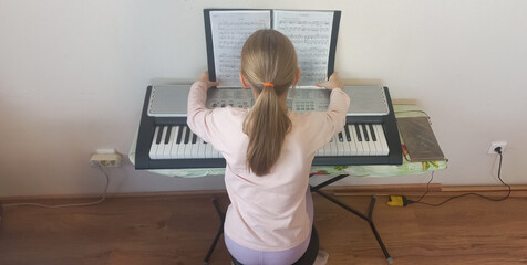 Young girl playing synthesizer and reading music notes indoors