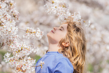 Naklejka premium Kids face with flower on the Spring. Child in blooming cherry garden on beautiful spring day. Happy child during spring blossom. Kid in flowered garden. Outdoor Portrait of child near blossoming tree.