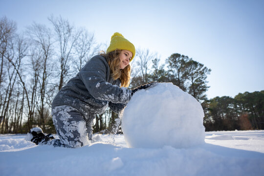 Smiling child building a snowman with snow on a sunny winter day. Happy girl playing in snow outdoors. Cute kid making a snowman. Child paly wit snow.