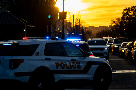 Police patrol blocks intersection. Sunset reflects emergency lights. Security presence reassures citizens. Law enforcement controls traffic. Capitol safety remains priority.