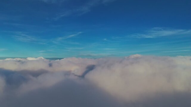 Stunning high-altitude shot soaring above a sea of dense cumulus clouds. Cinematic flight footage featuring a clear deep blue horizon, perfect for travel, heaven, and weather concepts.