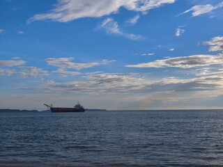 Cargo Ship Sailing on Sea at Sunset with Blue Sky and Clouds