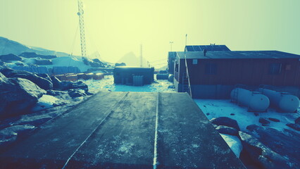 A stark winter scene unfolds with a research station surrounded by snow covered rocks. Towering equipment looms above, hinting at the challenges of this harsh environment.