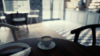 A person relaxes with a warm cup of coffee on a wooden table. Sunlight brightens the charming cafe, creating a cozy atmosphere. Pastries are nearby, inviting a sweet treat.