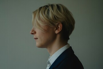  This is a close-up profile shot of a person with short, layered blonde hair. Their gaze is directed forward, and the lighting casts soft shadows on their neck and jawline. 