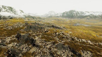 A stunning view of a barren landscape reveals rocky terrain, patches of grass, and towering mountains in the distance. A unique blend of colors signals the approach of twilight.