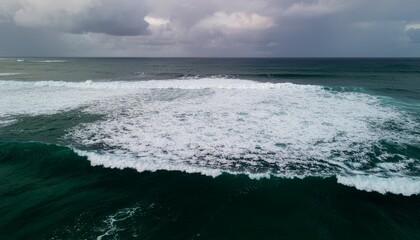 Stormy blue ocean waves crash on the sandy beach shore under a dark cloudy sky