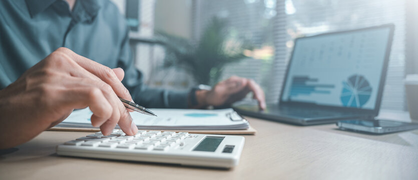 Close-up of hands using a calculator and reviewing financial data on a laptop, representing digital banking, loan calculation, credit analysis, and modern fintech transaction processes.