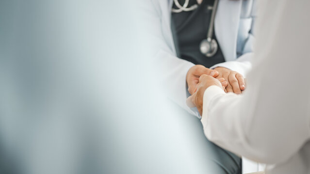 Close-up of a doctor holding a patient&rsquo;s hands, symbolizing medical consultation, compassionate care, professional support, and trust within a healthcare service setting.