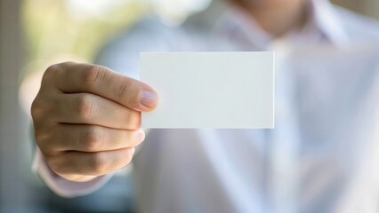 A hand holds a blank business card against a blurred background, ideal for showcasing branding or personal information.