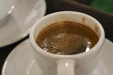 Close up of warm, aromatic black coffee in white ceramic cup. An invigorating espresso beverage on saucer perfect for morning break, offering simple comfort