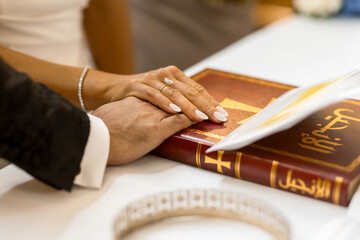 Close-up of bride and groom placing their hands on a ceremonial book during a wedding ritual. Elegant rings, polished nails and soft lighting highlight this intimate symbolic moment