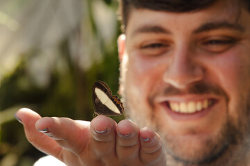 Smiling young man holding a butterfly on his hand in a tropical garden © Brenda