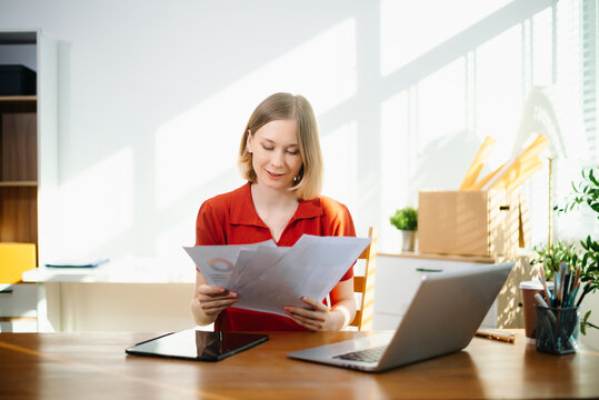 Caucasian woman reviewing documents at her home office desk with laptop. Perfect for themes of remote work, analysis
