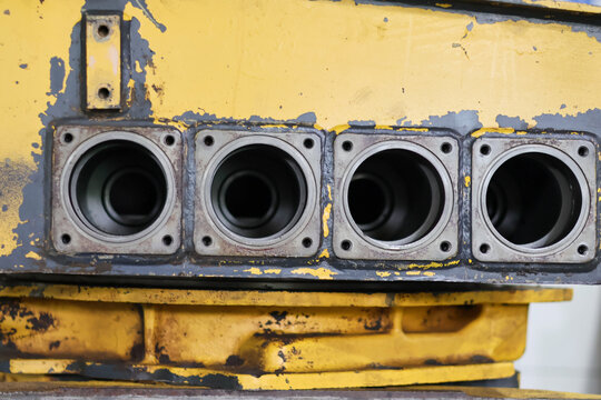 Row of four exposed cylindrical bores in a used, heavy-duty yellow machine casing, featuring square metallic flanges and internal cylinder liners, symbolizing industrial hydraulics and engine. - Powered by Adobe