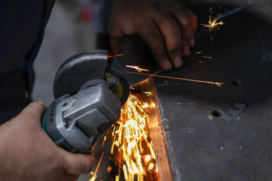 Close-up of a worker's hands using an angle grinder to cut metal, generating a dramatic shower of bright yellow and orange sparks, symbolizing heavy industry, construction, and metalworking